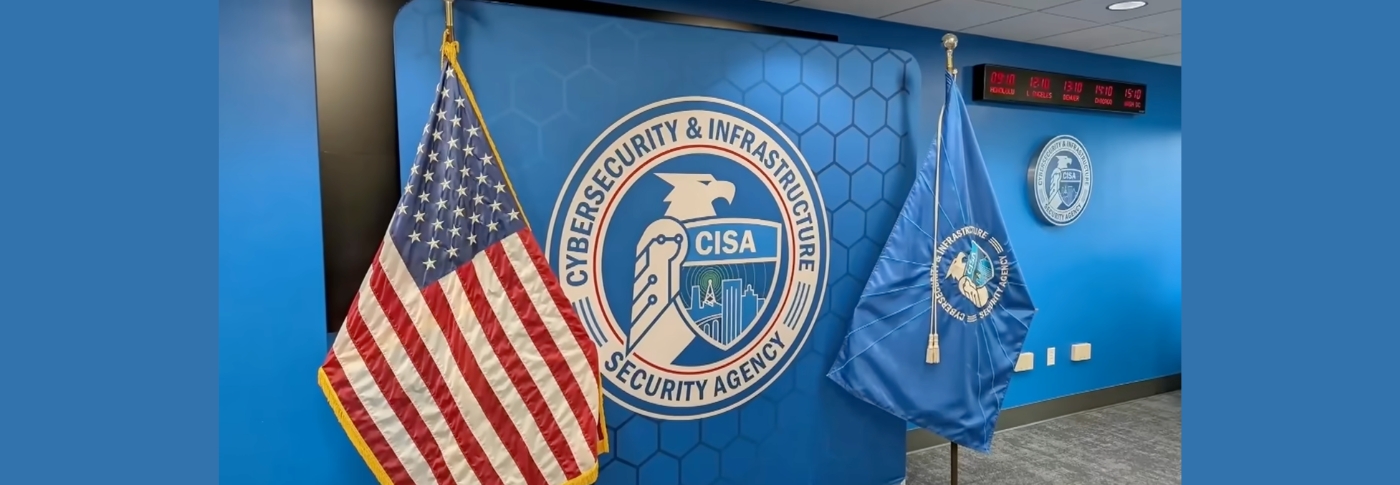 The CISA seal on a blue wall flanked by a U.S. flag and an agency flag inside the Cybersecurity and Infrastructure Security Agency.